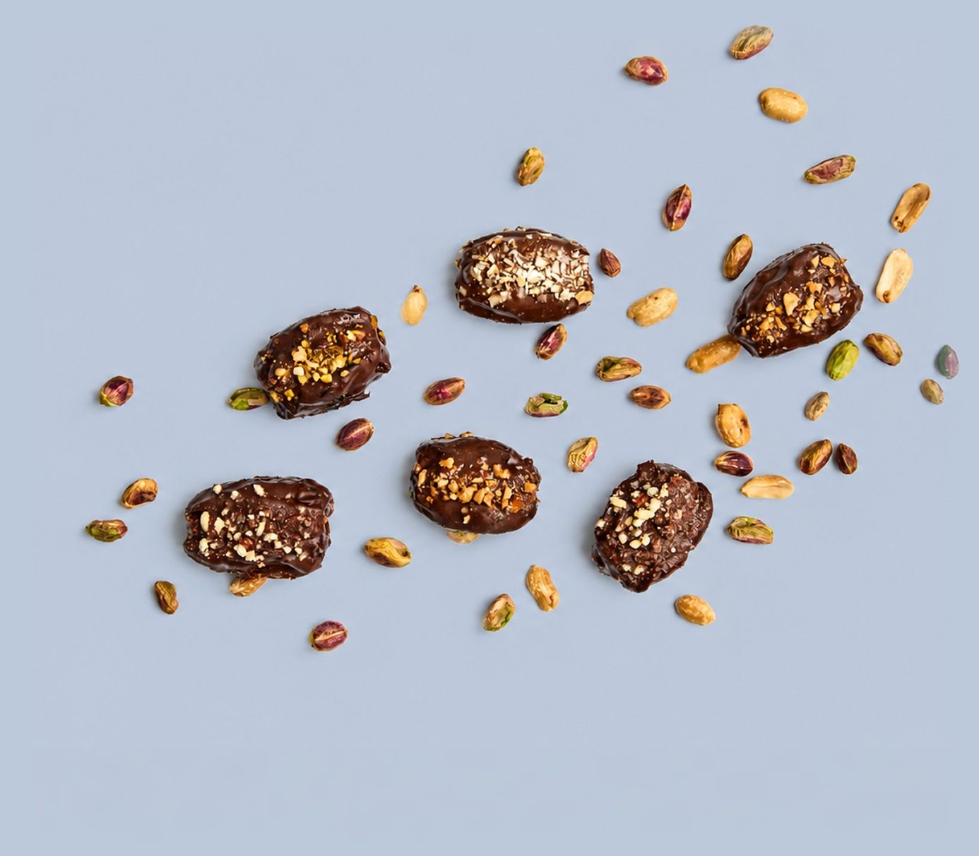 PITT stuffed Medjool dates scattered on blue with pistachio and peanut crumbs