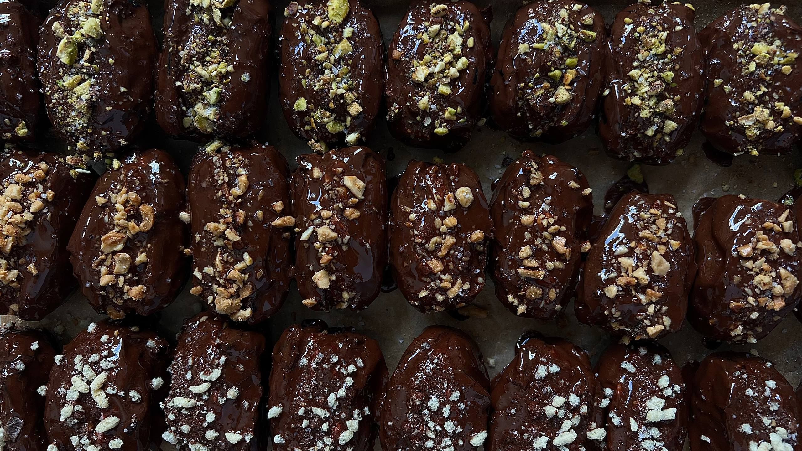 A tray of PITT dates fresh from the kitchen: rows of coconut, peanut and pistachio under dark chocolate