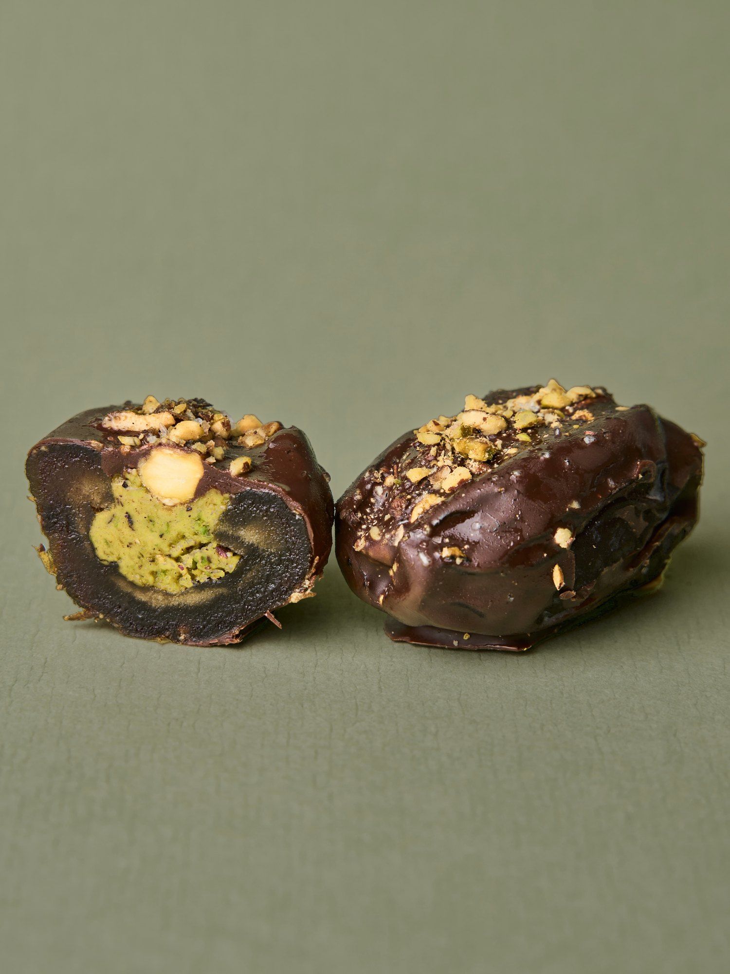 A PITT Pistachio date split open beside a whole one, the pistachio paste filling visible